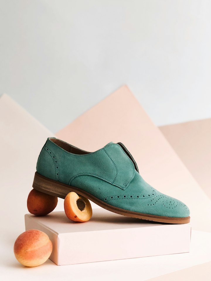 A sage green suede brogue shoe resting on peaches